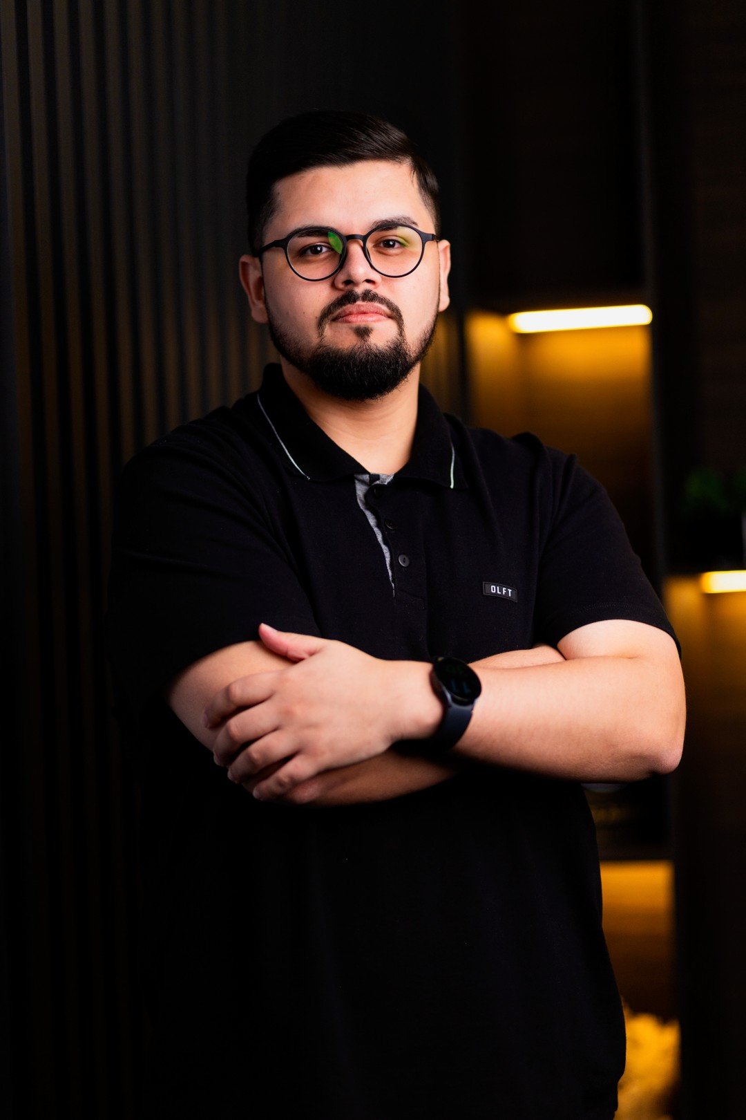 Retrato de Adoilson Cruz, de óculos e camisa preta, com os braços cruzados.